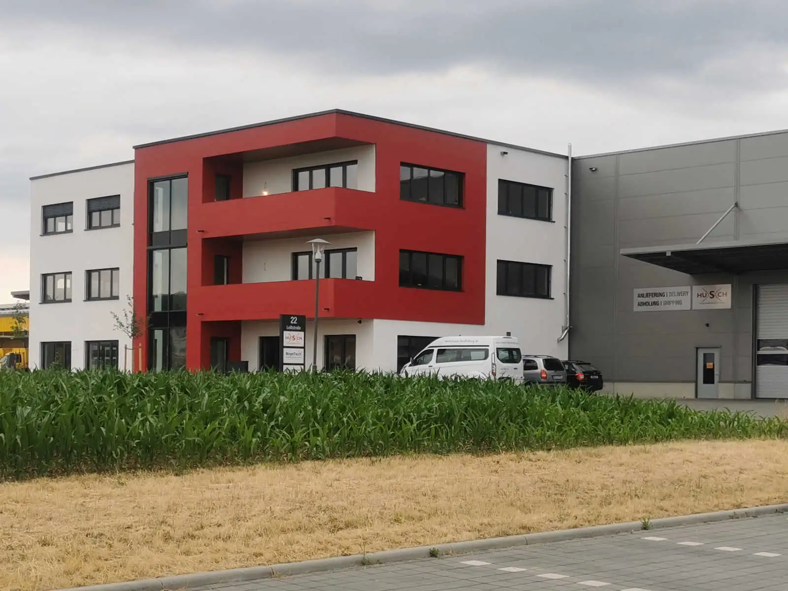 Firmengebäude von HUSCH Handhabungstechnik Foto einer hellgrauen Produktionshalle mit vorgesetztem Bürogebäude und roter Fassade