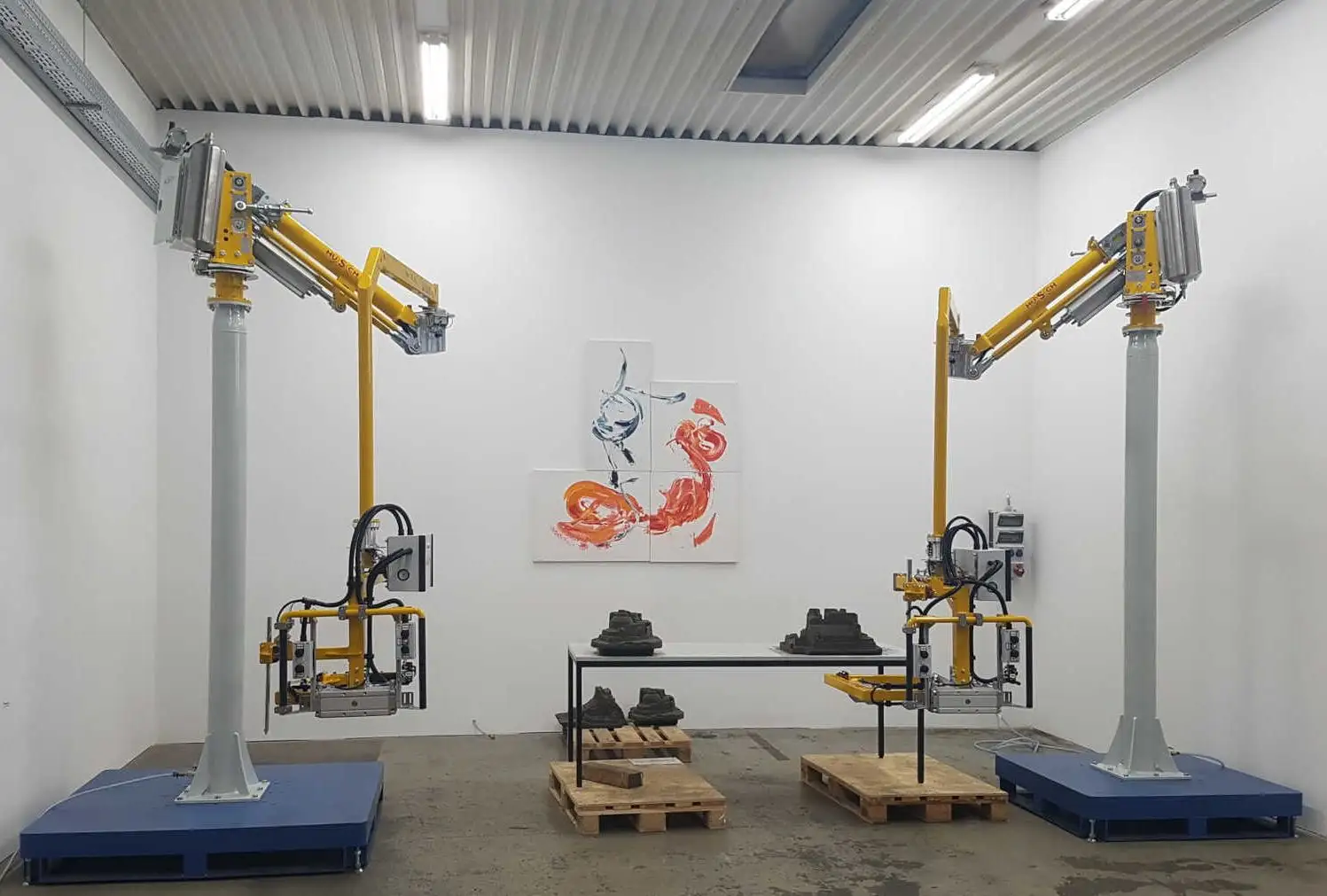 Foto von zwei Knickarm Manipulatoren für Sandkerne in einer Halle mit einem Kunstgemälde im Hintergrund