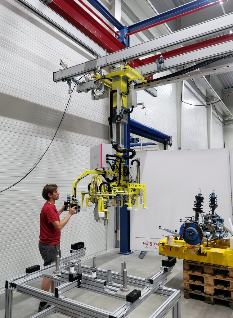 Ein Foto eines Manipulators mit gelber Hubsäule und komplexer Aufnahmevorrichtung für verschiedene Achstypen.