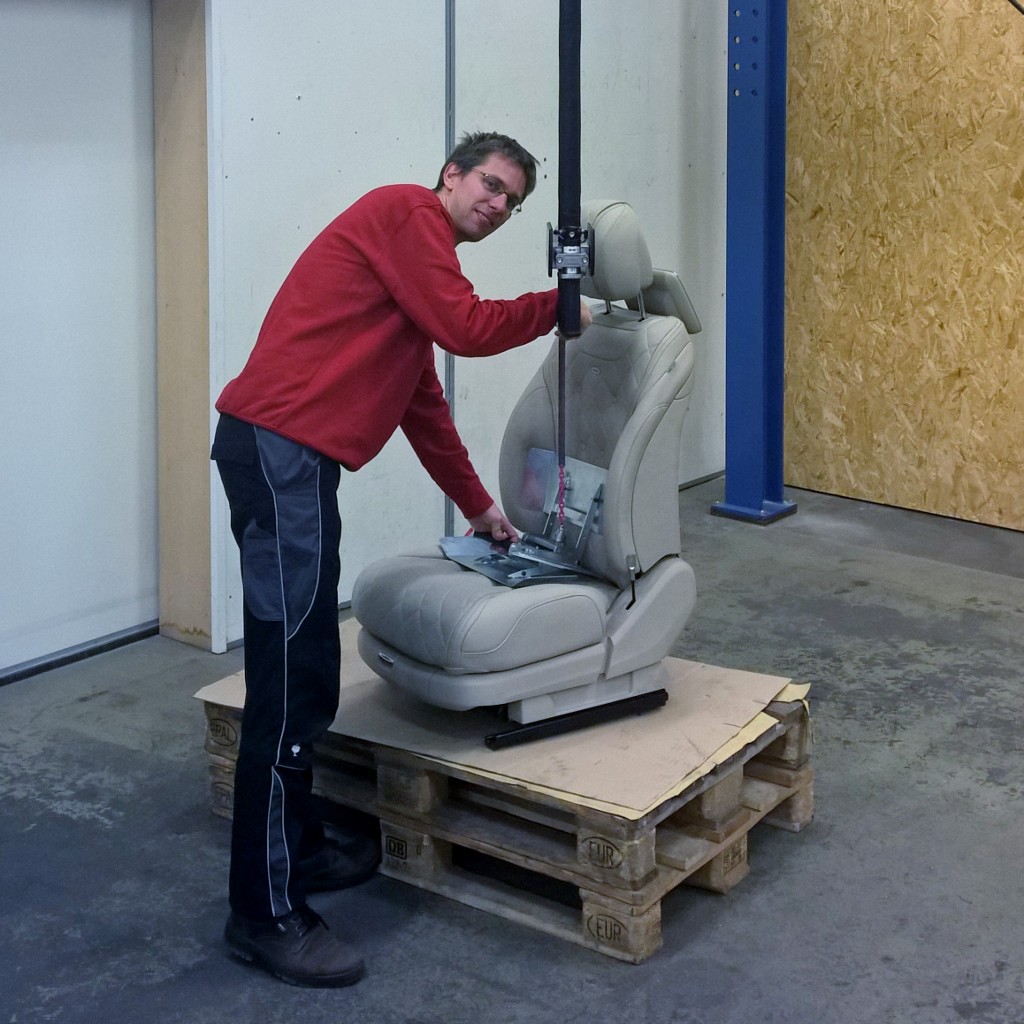 Ein Foto eines Manipulators mit Seil Hubgerät an welchen mittels einer Aufnahmevorrichtung ein Pkw- Sitz aufgenommen wird.