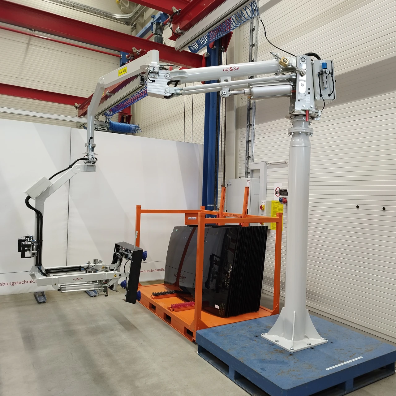 Ein Foto eines hellgrauen Knickarm Manipulators mit einer Sauggreifvorrichtung für Glasdächer von Automobilen.