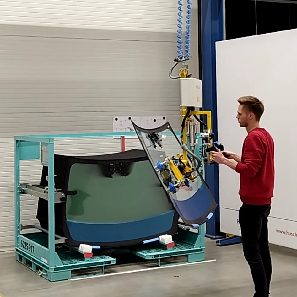 Ein Foto mit einer gelben Aufnahmevorrichtung mit Sauggreifern welche eine Frontscheibe eines Fahrzeugs aufgenommen hat.